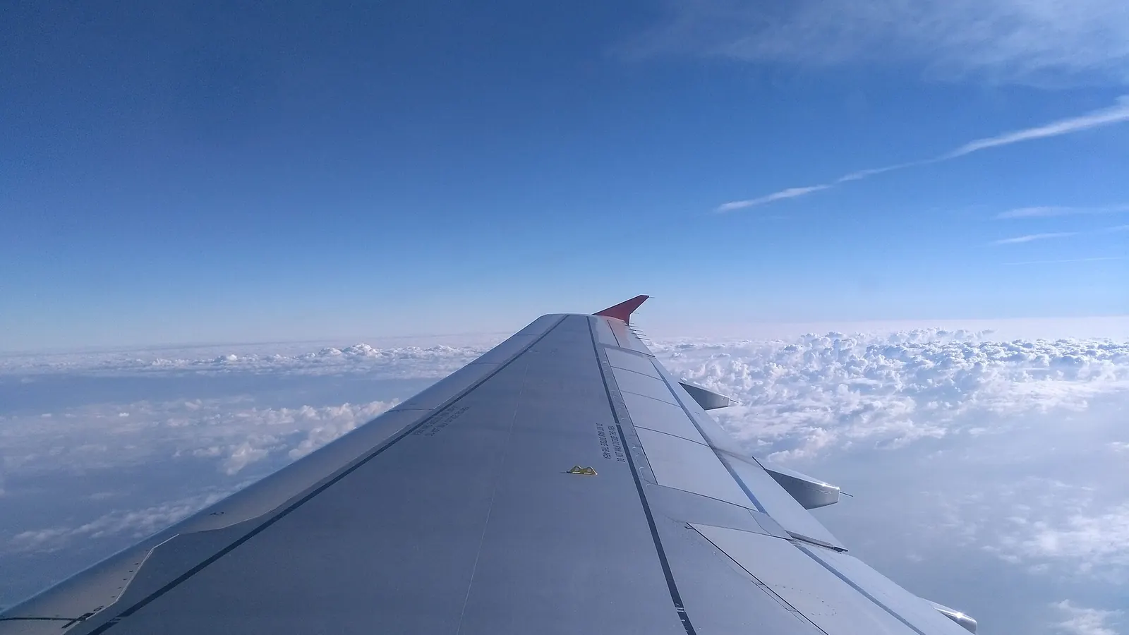 青空と雲海の上を飛ぶ旅客機の主翼